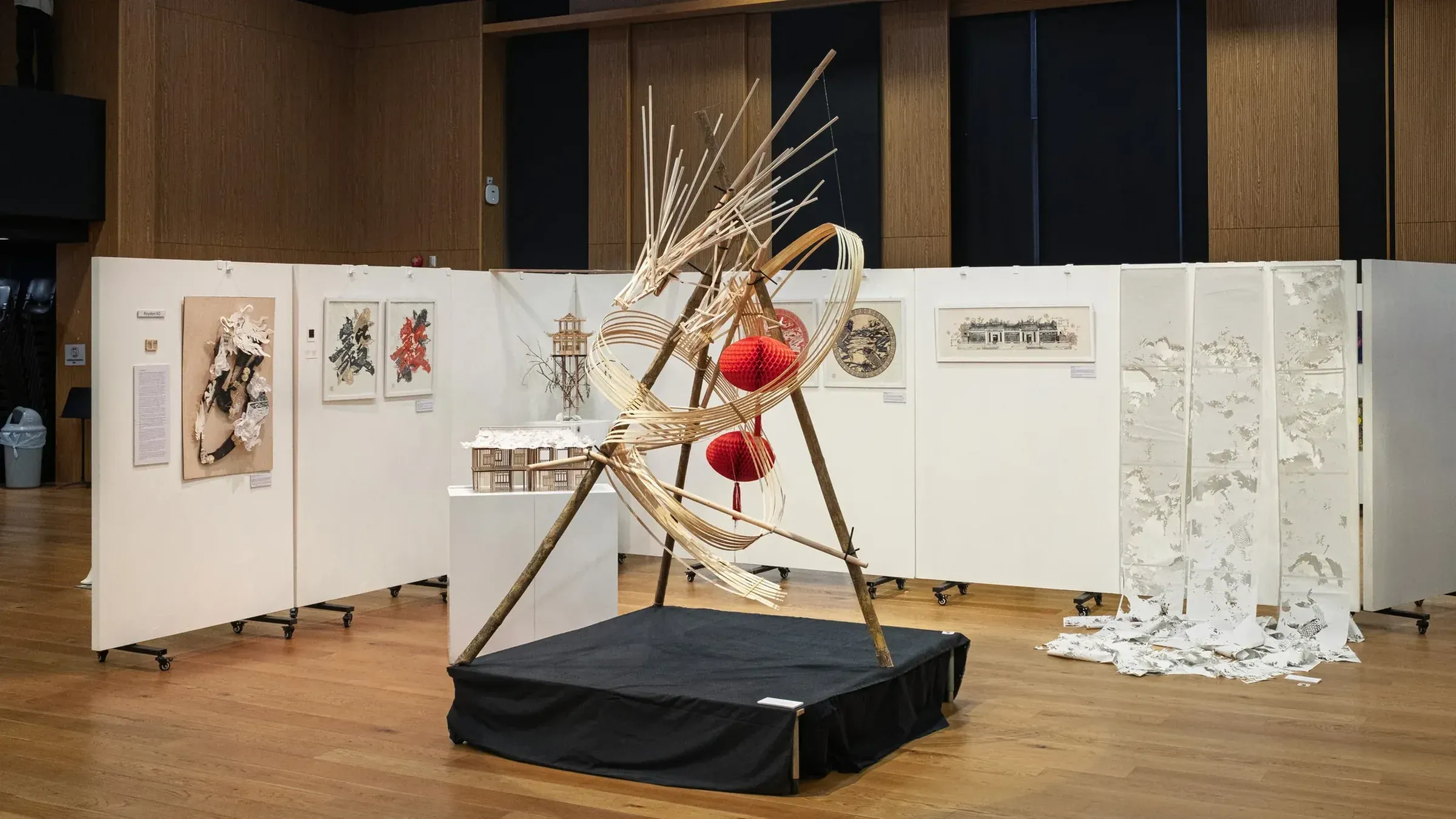 The Metamorphosis exhibition: the bamboo dragon on a black plinth, framed papercuts on white walls and a paper installation behind