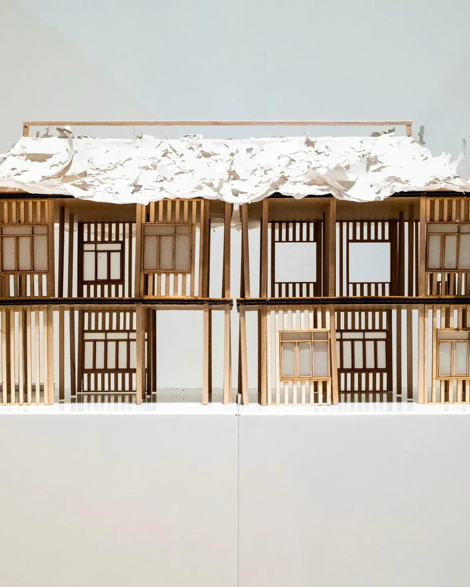 檐下 Under the Eaves, September 2024, balsa, newsprint and crepe paper, 20 × 56 cm: two storeys of shophouse fronts under a torn paper roof